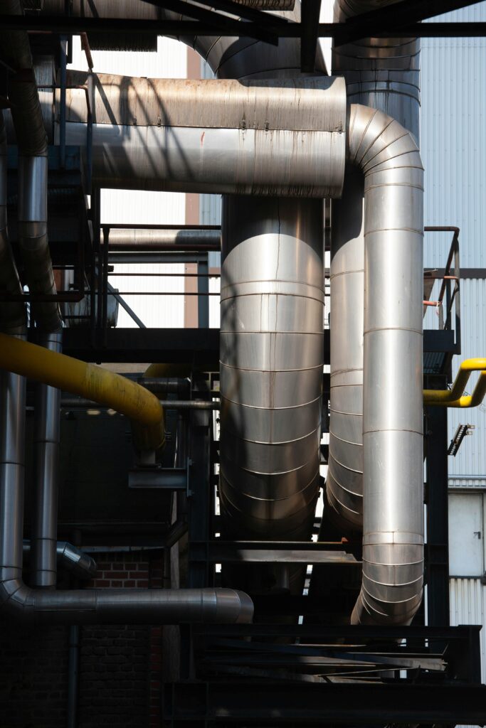 Intricate network of stainless steel pipes in an industrial complex under sunlight.